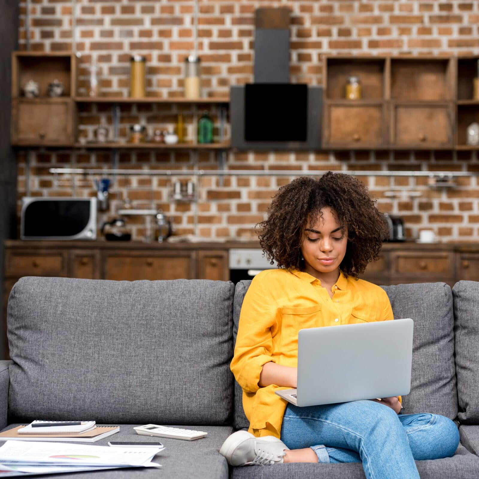 Image of a woman sitting on a couch working on a laptop.